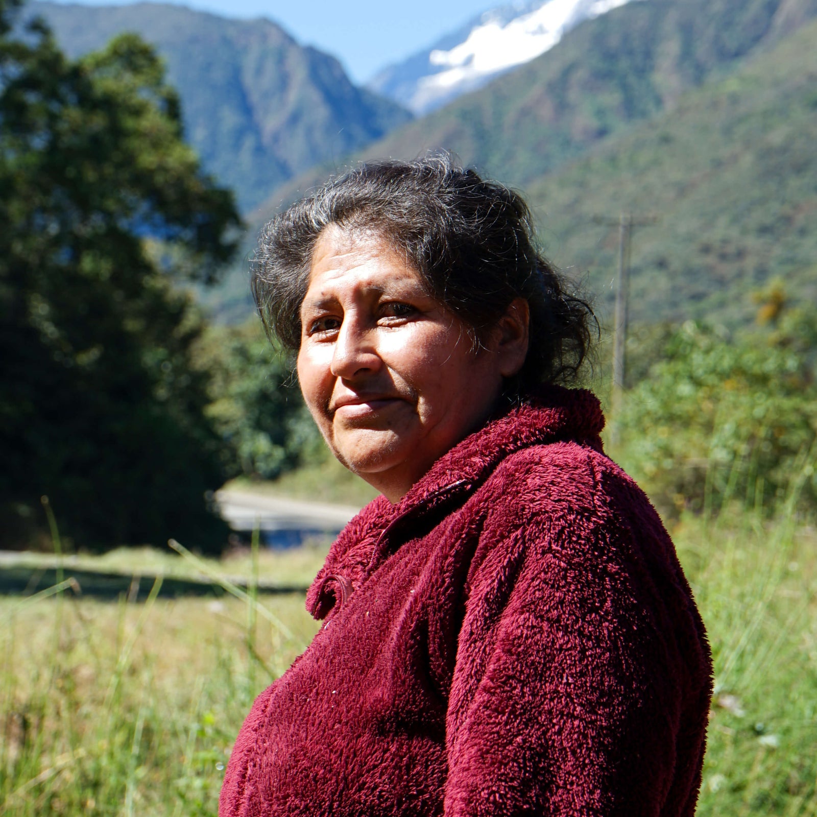 Woman in a red sweater standing in a grassy field with mountains in the background