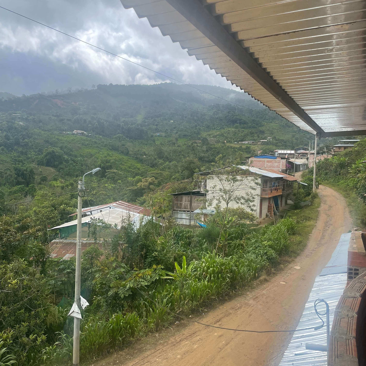 Village nestled in a lush green valley with a dirt road leading towards it.