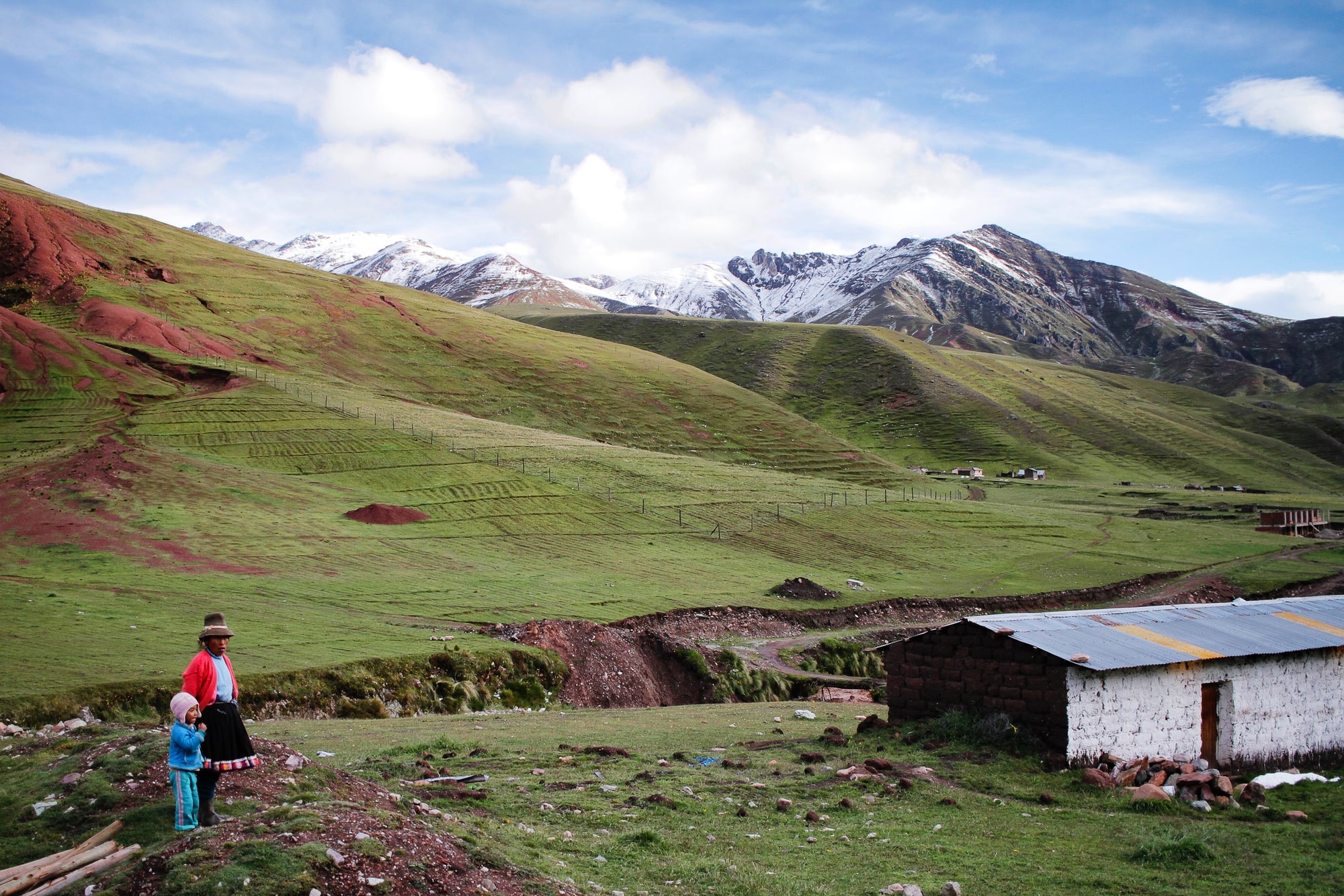 a picutre of a women and child by their house in the andes overlooking a mountain with snow on top